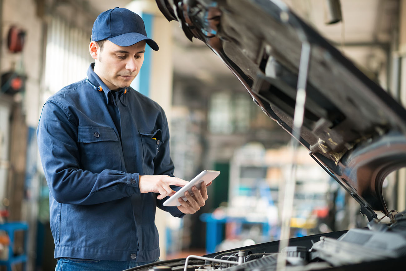 Car Mechanic A mechanic dressed in blue checking the car engine and holding an ipad